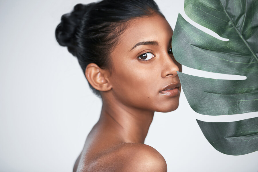 Bioestimulador Sculptra - Mujer con piel radiante posando junto a una hoja tropical
