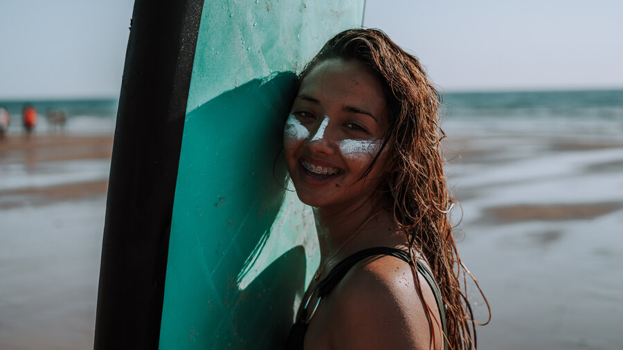 Láser CO2 Fraccionado Cómo Funciona cuidados - Joven surfista sonriente en la playa con tabla y protector solar