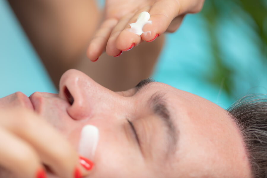 Skin booster beneficios cuidados - Aplicación de crema facial en el rostro de un hombre durante tratamiento de cuidado de la piel.