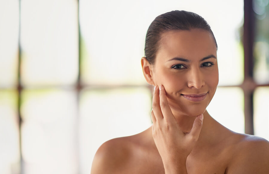 Skin booster beneficios resultados inmediatos - Mujer sonriendo mientras toca suavemente su rostro