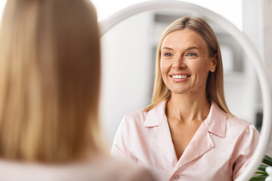Tratamientos Sculptra testimonios - Mujer sonriendo frente al espejo