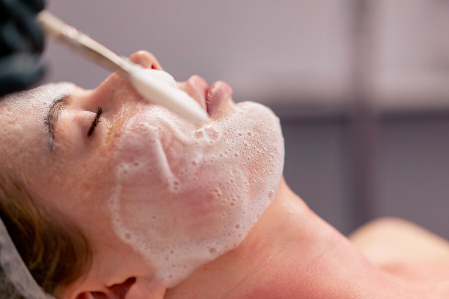 Beneficios del hydrafacial comparativa - Aplicación de espuma facial con brocha durante tratamiento estético