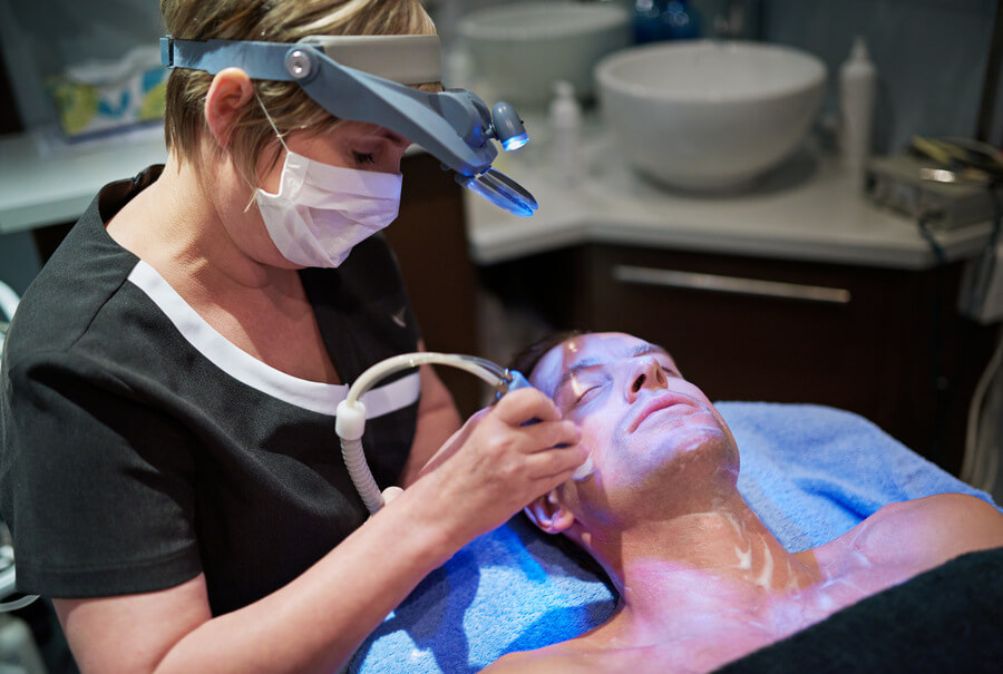 Beneficios del hydrafacial cuidados - Especialista realizando tratamiento facial a un hombre con luz azul y equipo dermatológico.