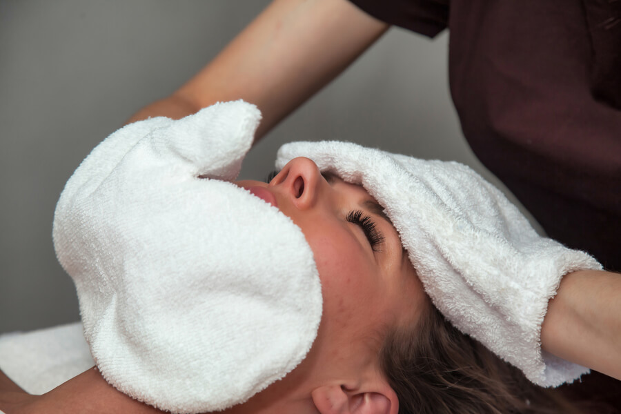 Beneficios del hydrafacial - Mujer recibiendo tratamiento facial con toalla caliente en el rostro