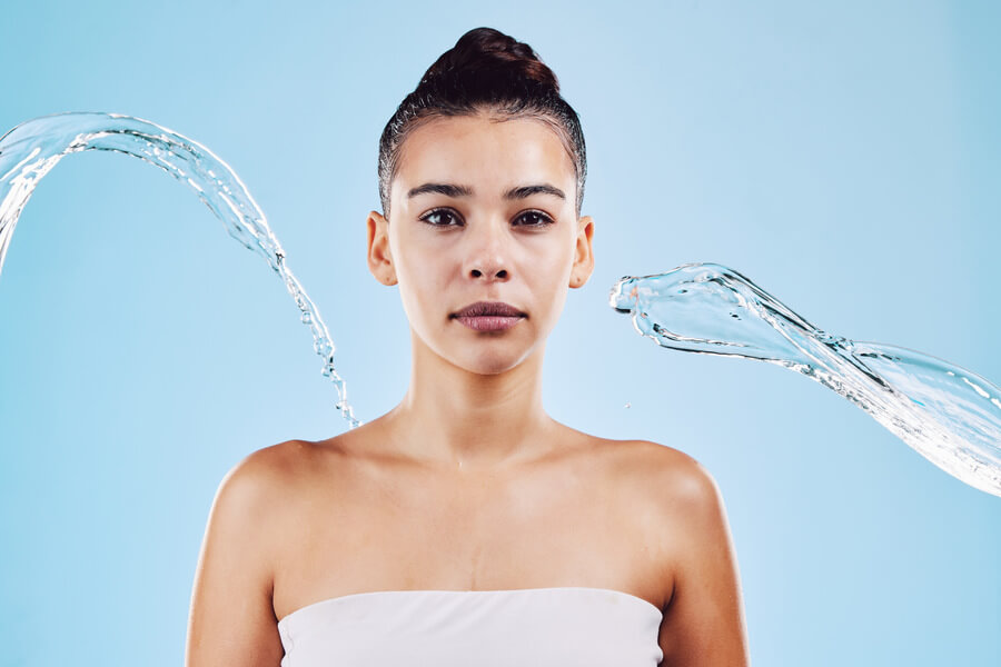 Harmonyca tratamiento facial cuidados - Mujer con la piel mojada rodeada de chorros de agua sobre fondo azul.