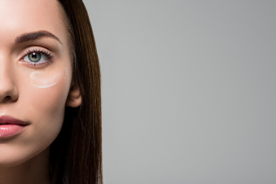 Harmonyca tratamiento facial sesiones - Rostro de mujer con crema debajo del ojo izquierdo, fondo gris claro