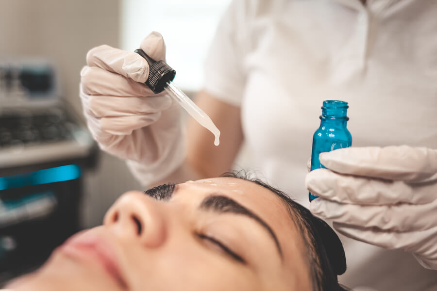 Harmonyca tratamiento facial tratamiento - Profesional aplicando suero facial con gotero en la frente de una mujer durante un tratamiento estético