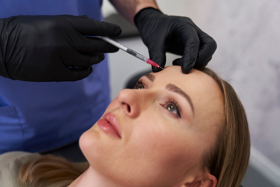 Nctf 135 ha antes y después beneficios - Mujer recibiendo inyección estética en la frente aplicada por un especialista con guantes negros.