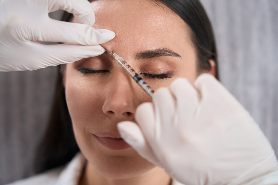 Nctf 135 ha antes y después quienes - Mujer con ojos cerrados recibiendo inyección estética en la frente por un especialista con guantes blancos.