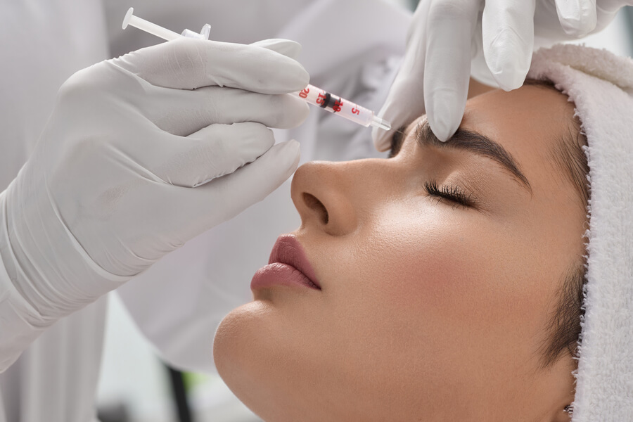 Nctf 135 ha antes y después - Mujer recibiendo inyección estética en la frente aplicada por un especialista con guantes blancos.