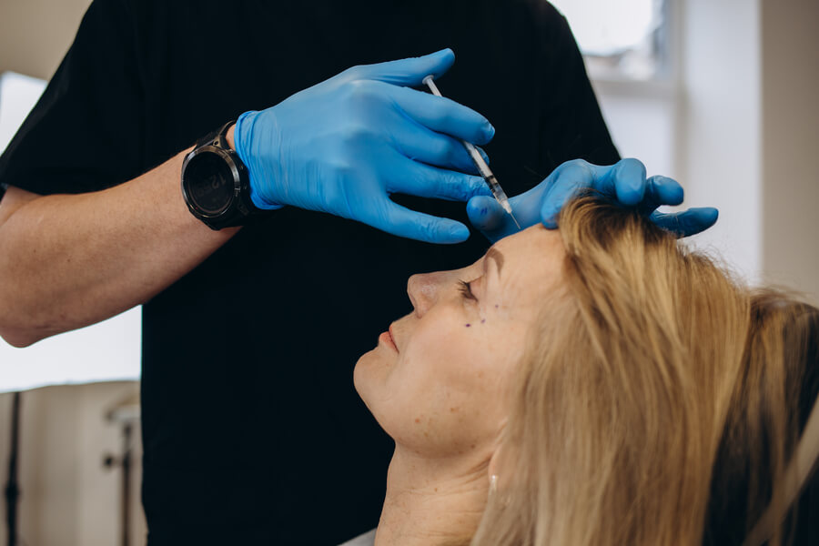 Mujer recibiendo aplicación de bótox en la frente por un profesional con guantes azules.