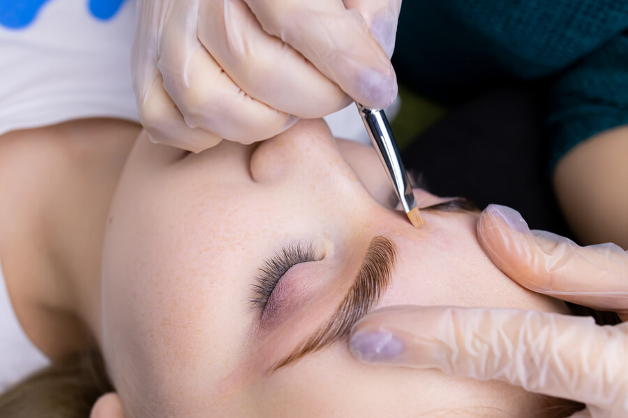 Cuanto dura la micropigmentación de cejas conclusion - Mujer con los ojos cerrados durante un procedimiento estético en las cejas realizado con pincel por un especialista con guantes.