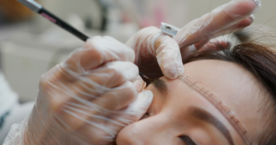 Cuanto dura la micropigmentación de cejas - Mujer en procedimiento de diseño o maquillaje de cejas realizado por un especialista con guantes.