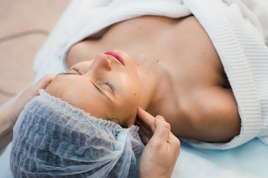 Que es bótox comparación - Mujer recibiendo masaje facial relajante con los ojos cerrados y gorro quirúrgico.
