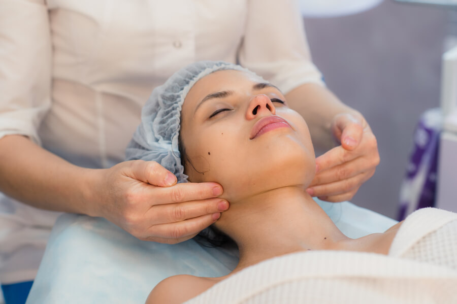 Que es bótox conclusión - Mujer recibiendo masaje en el rostro y cuello con los ojos cerrados y gorro quirúrgico.
