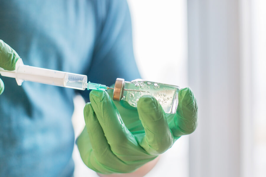 Que es bótox introducción - Mano con guantes verdes extrayendo líquido de un vial con una jeringa.