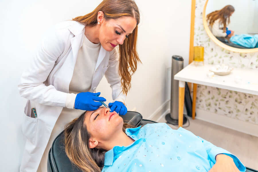 Radiesse para qué sirve beneficio - Profesional aplicando tratamiento estético en el rostro de una mujer recostada.