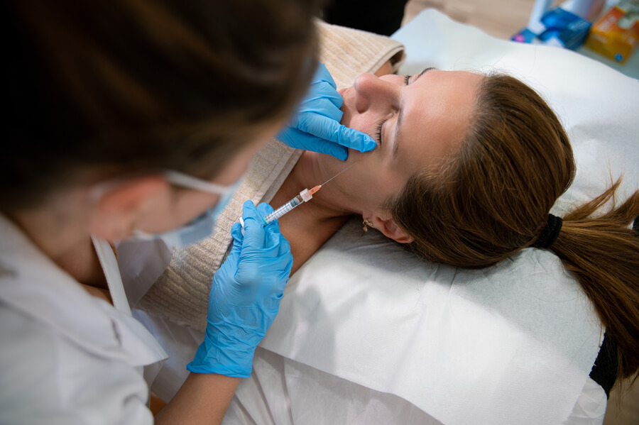 Radiesse para qué sirve cuidado - Profesional aplicando inyección estética en el rostro de una mujer recostada.
