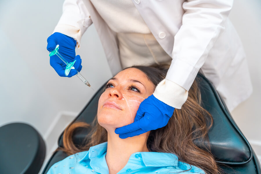Radiesse para qué sirve proceso - Profesional aplicando inyección estética en el rostro de una paciente recostada.